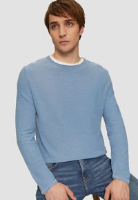 Himmelblaues Langarmcrewneck-Sweatshirt aus weichem Material mit einem weißen Innenkragen und einem lässigen Schnitt, kombiniert mit dunklen Jeans.