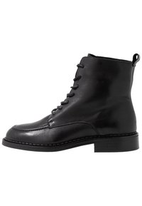 Botas de cuero negro hasta el tobillo con acabado suave, puntera redonda, diseño con cordones, suela gruesa y detalles cosidos a lo largo de los bordes.