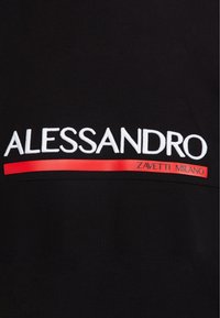 Camiseta negra con texto bordado en blanco "ALESSANDRO" sobre una franja roja horizontal con "ZAVETTI MILANO" impreso en blanco.