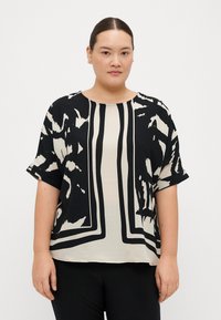 Blusa a maniche corte in nero e crema con motivi astratti, caratterizzata da un colletto rotondo e una vestibilità ampia. Tessuto morbido e leggero.