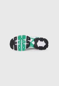 White athletic shoe sole featuring a black and green rubber outsole with multi-directional grooves and textured patterns for traction.