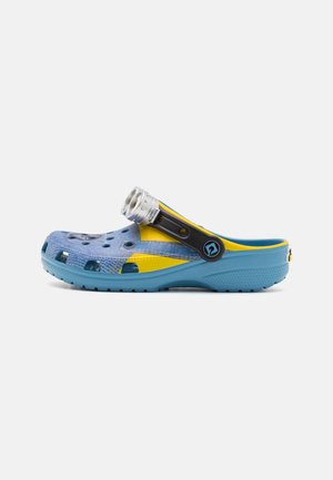 Sabot bleu clair et jaune avec des trous de ventilation et une bride noire réglable avec une fixation lumineuse circulaire argentée.
