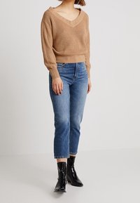 Beige knit sweater with a V-neck and long sleeves, paired with mid-rise blue jeans. Black ankle boots with a glossy finish.