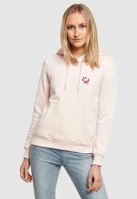 Felpa rosa con tasca frontale, cordini e un piccolo emblema rosso sul petto. Realizzata in tessuto morbido e strutturato.