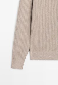 Jasnobeżowy prążkowany sweter z długimi rękawami, o miękkiej fakturze i dopasowanych ściągaczach. Dół swetra jest prosty i lekko elastyczny.