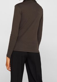 Top marrone a maniche lunghe con colletto alto, design aderente e texture morbida, abbinato a pantaloni neri larghi.