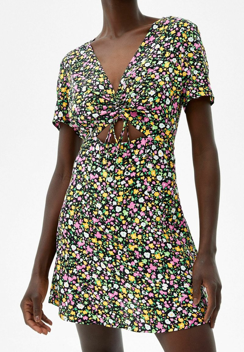 Krótka sukienka w kwiaty z czarnym tłem, zdobiona kolorowymi różowymi, żółtymi i zielonymi kwiatami. Ma dekolt w kształcie litery V, krótkie rękawy oraz wycięcia.