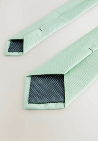 Cravate vert menthe avec une surface texturée et un revers bleu marine comportant un motif à pois, présentant des extrémités effilées et des coutures nettes.