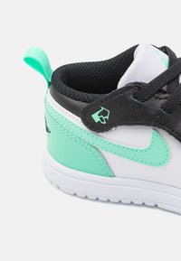 Schwarze und weiße Sneaker mit mintgrünen Akzenten, strukturiertem Obermaterial, gepolstertem Kragen und Zuglasche für einfaches An- und Ausziehen.