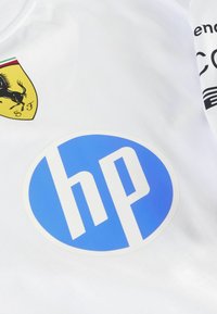 Tricou sportiv alb cu un emblema de cal negru pe un fundal galben și un logo circular albastru cu text alb "hp".