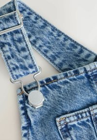 Bretelle de salopette en denim bleu avec boucle et bouton en métal, avec un motif imprimé léopard sur le tissu.