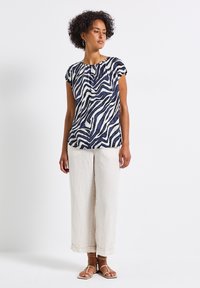 Top a maniche corte blu marino e bianco con una stampa, realizzato in tessuto morbido e leggero, abbinato a pantaloni larghi color crema e sandali marroni.