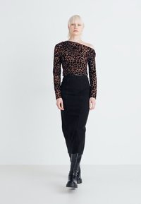 Majica z dolgimi rokavi in off-shoulder dizajnom v leopardjem vzorcu, združena z visokim črnim svilenim krilom. Model nosi črne gležnjarje.