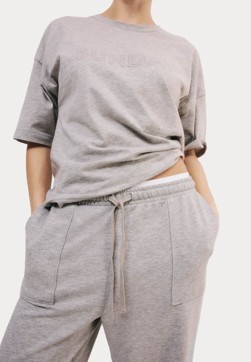Lichtgrijze oversized t-shirt met de tekst "SUNDAY" en bijpassende grijze joggingbroek met een elastische tailleband en zijzakken.