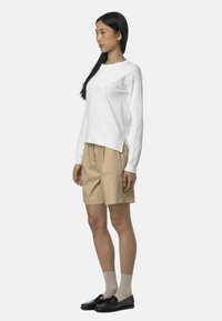 Maglione bianco a maniche lunghe, pantaloni corti beige e mocassini neri con calzini beige, che mostrano un fit rilassato e un design semplice.