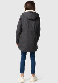 Black hooded jacket with a faux fur collar, featuring a drawstring, and a slightly fitted silhouette. Worn over blue jeans and sneakers.