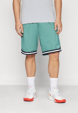 Türkise Basketball-Shorts mit einem schwarz-weiß gestreiften Saum, aus Netzstoff gefertigt. Kombiniert mit weißen Turnschuhen und Socken in Crew-Länge.