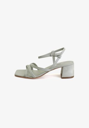 Sandale en cuir vert clair avec un bout carré, plusieurs lanières croisées, boucle à la cheville et un talon épais. Texture lisse et design minimaliste.