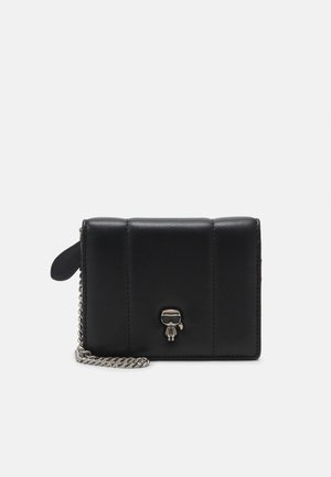 Schwarze Lederbörse mit gestepptem Design, silberner Kettenriemen und einem dekorativen Anhänger mit einer Figur, die Sonnenbrillen trägt.