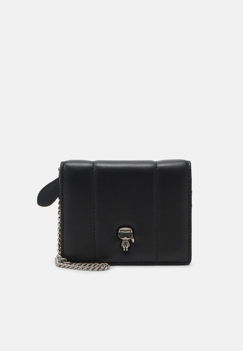 Portafoglio in pelle nera con design trapuntato, tracolla in catena argentata e un charm decorativo con una figura che indossa occhiali da sole.