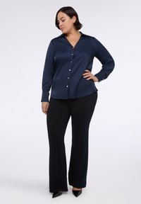 Tmavě modrá saténová košile na knoflíky s límečkem, dlouhými rukávy a stříbrnými knoflíky, doplněná o černé rozšířené kalhoty a černé špičaté lodičky.