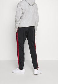 Tenue de sport comprenant un sweat à capuche gris et un pantalon noir avec des bandes rouges sur les côtés. Des baskets blanches complètent le look.