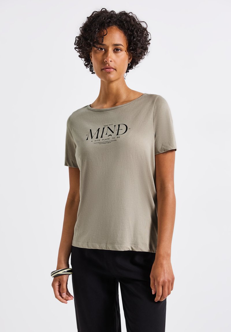 Oliivivärvi lühikeste varrukatega T-särk pehmest kangast, millel on must graafikaprindiga "MIND" tekst. Loodud vabaks istuvuseks, ümmargune kaelus.