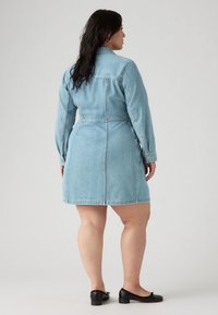 Φόρεμα τζιν σε ανοιχτό μπλε, με μακριά μανίκια, εφαρμοστή μέση και φουσκωτό φουστάνι. Διαθέτει κουμπωτές μανσέτες και γιακά. Συνδυάζεται με μαύρες μπαλαρίνες.