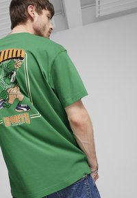 Camiseta de algodón verde con un estampado gráfico de un personaje de baloncesto en la parte posterior, de mangas cortas y un ajuste relajado.