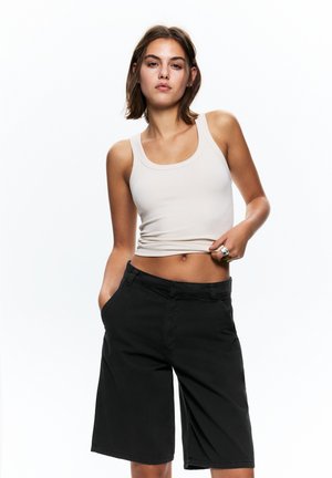 Pantaloni corti neri in tessuto, con tasche frontali e taglio dritto. Abbinati a un top aderente beige chiaro, con una texture piatta a coste.