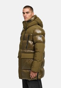 Olijfgroene pufferjack met een glanzende afwerking, verstelbare capuchon, ritszakken en een gewatteerde textuur, met een embleem op de mouw.