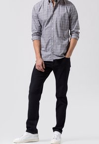 Camisa de cuadros en azul, gris y blanco, combinada con jeans oscuros y zapatillas blancas. Presenta mangas largas y un corte relajado.