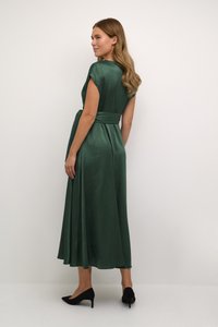 Green satin dress with a flowing design, short sleeves, and a waist tie. Back view reveals a midi length and smooth texture. Black heels complete the look.