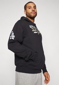 Felpa nera con tasca frontale, con i design "LOS" e "ANGELES" in vari colori. Polsini e orlo elasticizzati, tessuto morbido. Pantaloni felpa grigi.
