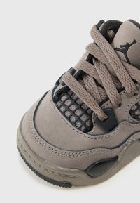 Graue Wildledersneaker mit schwarzen Netz-Elementen, Gummisohle, dicken Schnürsenkeln und einem kleinen Logo auf der Zunge. Abgerundete Zehenpartie und strukturierte Oberfläche.