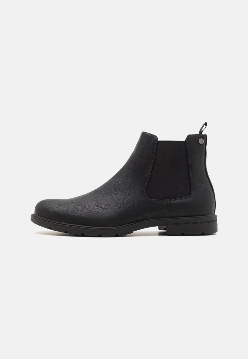 Bottine Chelsea en cuir noir avec panneaux latéraux élastiques, languette au talon et semelle basse superposée sur fond blanc.