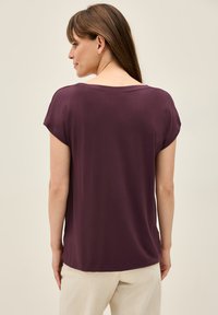 Haut à manches courtes, ample, en tissu bordeaux profond. Il présente un col rond et une texture douce, associé à un bas crème léger.