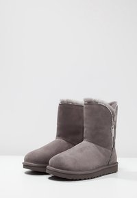 Šedé semišové kotníkové boty s měkkou, chlupatou podšívkou, bočním zipem a ozdobami z broušených kamínků. Plochá gumová podrážka a zaoblená špička.