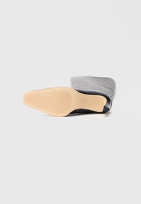 Bottines noires à finition brillante avec un tige grise texturée. La semelle est en caoutchouc avec des rainures horizontales pour une meilleure adhérence.