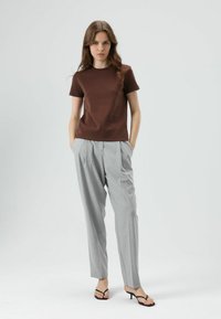 Braunes T-Shirt mit kurzen Ärmeln, kombiniert mit hellgrauen, locker sitzenden Hosen mit Vorderfalten. Schwarze Riemchensandalen runden das Outfit ab.