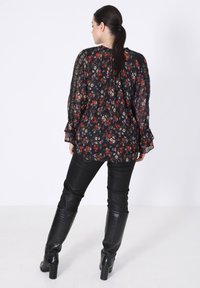 Black floral blouse with sheer fabric, ruffled sleeves, and multicolored floral pattern paired with high-waisted black faux leather pants and boots.