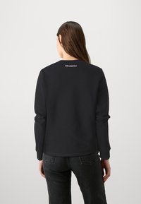 Čierna mikina s dlhými rukávmi, z ľahkého materiálu, s okrúhlym výstrihom a malým logom "KARL LAGERFELD" na zadnej strane výstrihu.
