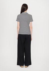 Ribaga lühikeste varrukatega topp musta ja valgega, koos vaba lõikega tumedate pükstega. Riietusel on mugav lõige ja pehme kangas.