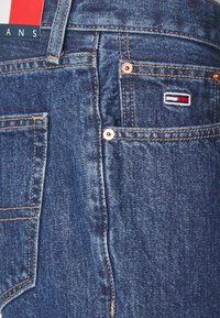 Jeans de denim azul con herrajes de cobre, parche de logo bordado, costuras en contraste y un diseño clásico, con bolsillos laterales y traseros.
