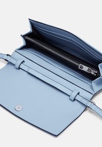 Jasnoniebieska skórzana torebka z zamkiem błyskawicznym w środku, o płaskim wzorze, regulowanym pasku i gładkim wykończeniu. Posiada okrągłe zapięcie na zatrzask.