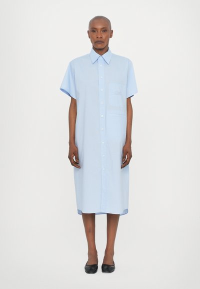 Vestito camicia azzurro chiaro con maniche corte, colletto a punta e taschino sul petto. Tessuto liscio e leggero con una vestibilità morbida.