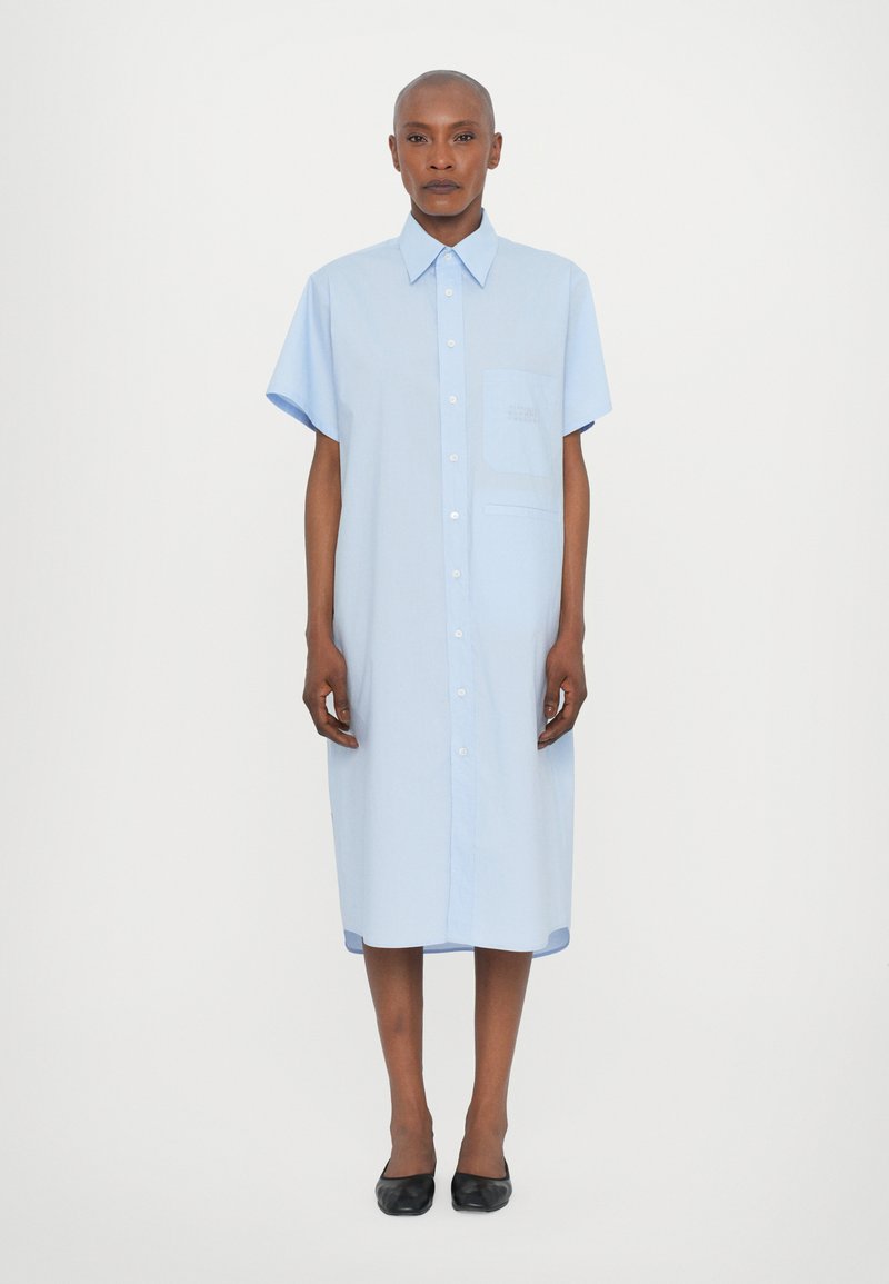 Vestito camicia azzurro chiaro con maniche corte, colletto a punta e taschino sul petto. Tessuto liscio e leggero con una vestibilità morbida.
