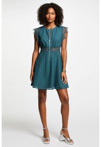 Türkises Kleid mit Spitzenakzenten, Reißverschluss vorne, kurzärmelig, strukturiertes Lochmustergewebe, ausgestellter Rock, kombiniert mit silbernen Absätzen.