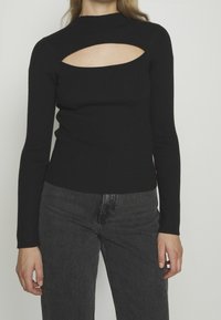 Svart ribbade långärmad topp med hög krage och rektangulär utskärning vid bröstet. Kombinerad med mörkgrå jeans.