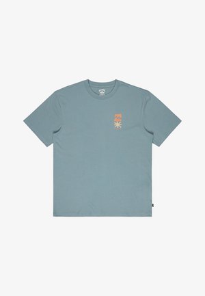 Světle modré bavlněné tričko s krátkými rukávy, na levé straně hrudi má malý oranžový grafický motiv. Na boku je viditelná značka.